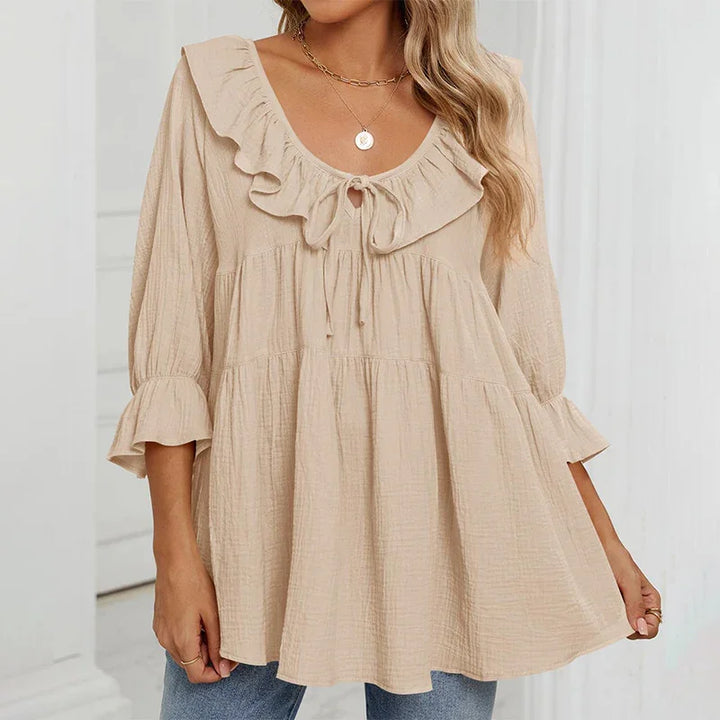 Woman wearing beige ruffle neckline blouse with tie front and 3/4 sleeves, paired with blue jeans