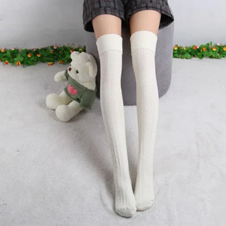 Person wearing white knee-high knit socks sitting on gray surface with a teddy bear nearby