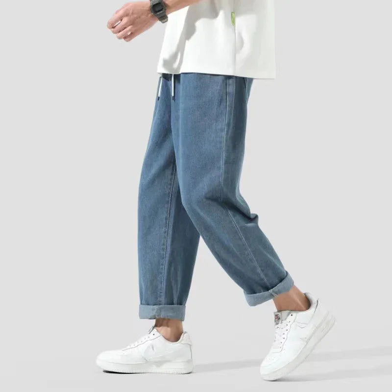 Person wearing cuffed blue denim jeans and white sneakers walking on plain background