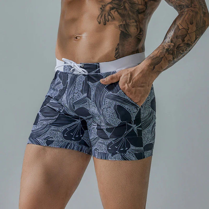 close-up of muscular man wearing black and white floral pattern swim trunks with side pocket and drawstring