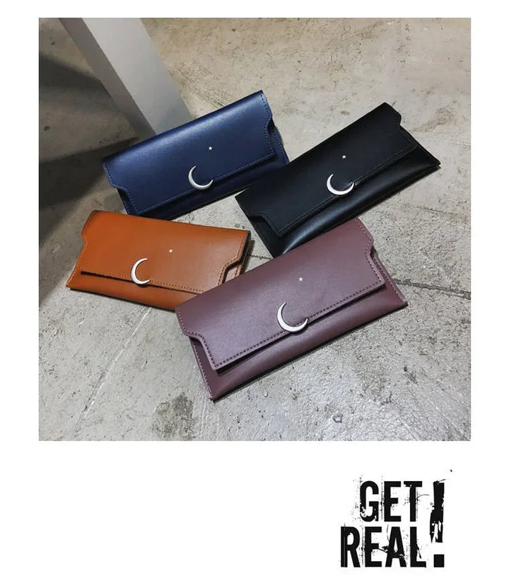 Four leather wallets in blue, black, brown, and purple with crescent moon and star accents on a concrete surface