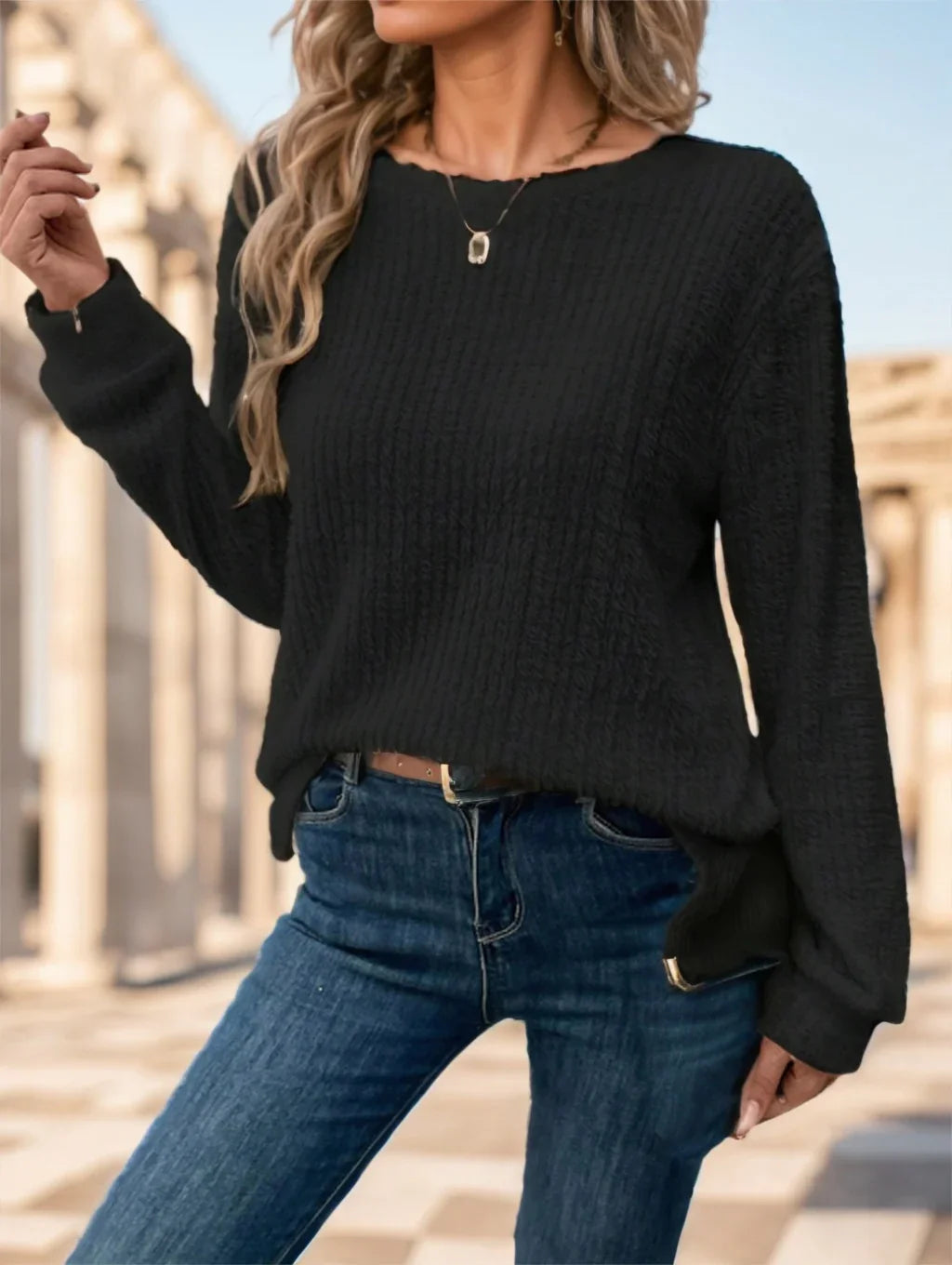 Woman wearing a black textured sweater and blue jeans in an outdoor urban setting with architectural columns