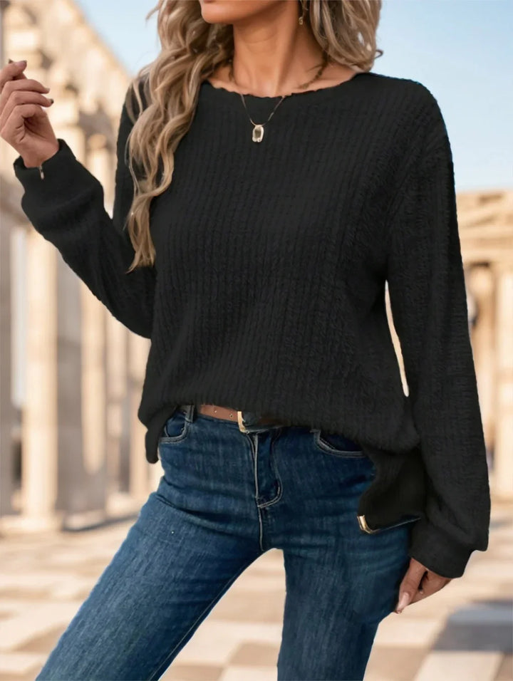 Woman wearing black textured sweater and blue jeans in outdoor architectural setting