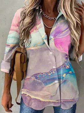 Woman wearing colorful pastel marble print button-up shirt with rolled sleeves and layered silver necklaces
