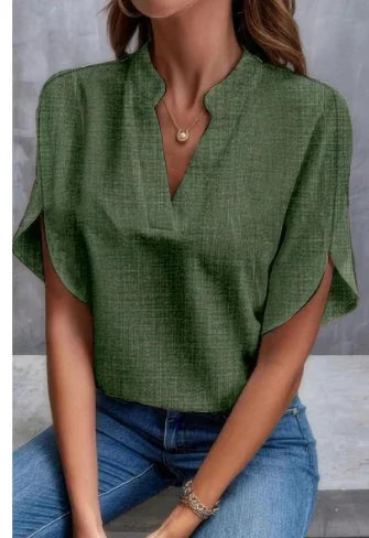 Woman wearing a green textured V-neck blouse with short sleeves and blue jeans, accessorized with gold necklace and bracelet