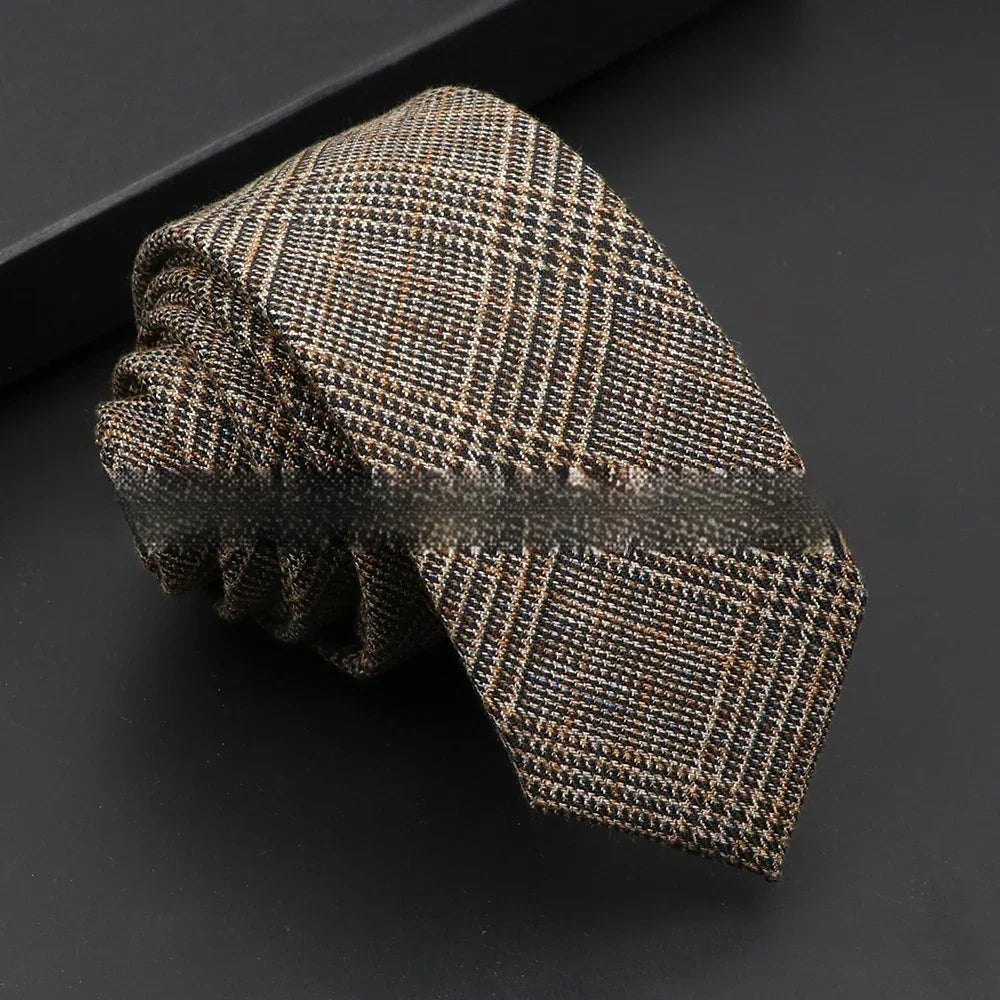 Rolled brown and black plaid men's wool tie on black surface with black box background