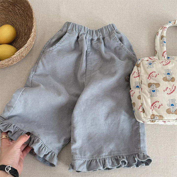 Light blue corduroy shorts with ruffle hem, beige teddy bear print bag, and basket with lemons