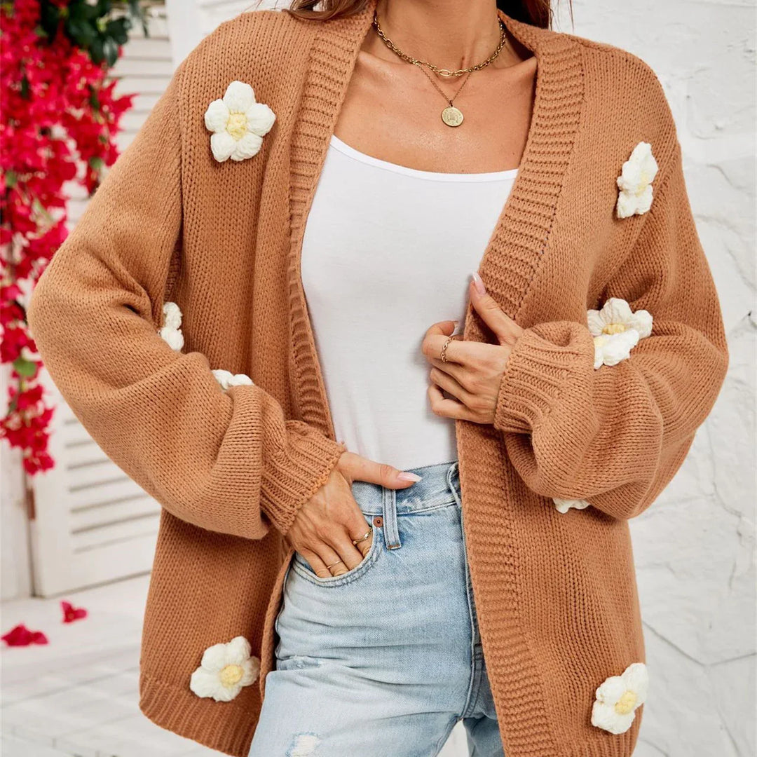 Woman wearing brown knit cardigan with white flower appliqués over white top and light blue jeans