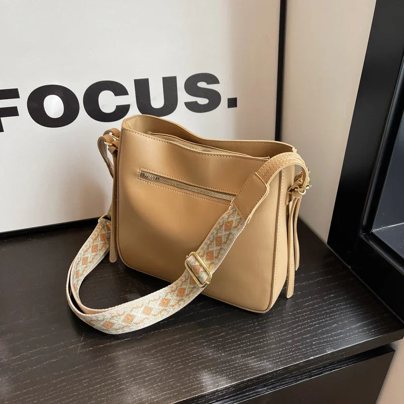 Tan leather shoulder bag with patterned adjustable strap on dark wooden surface next to Focus sign