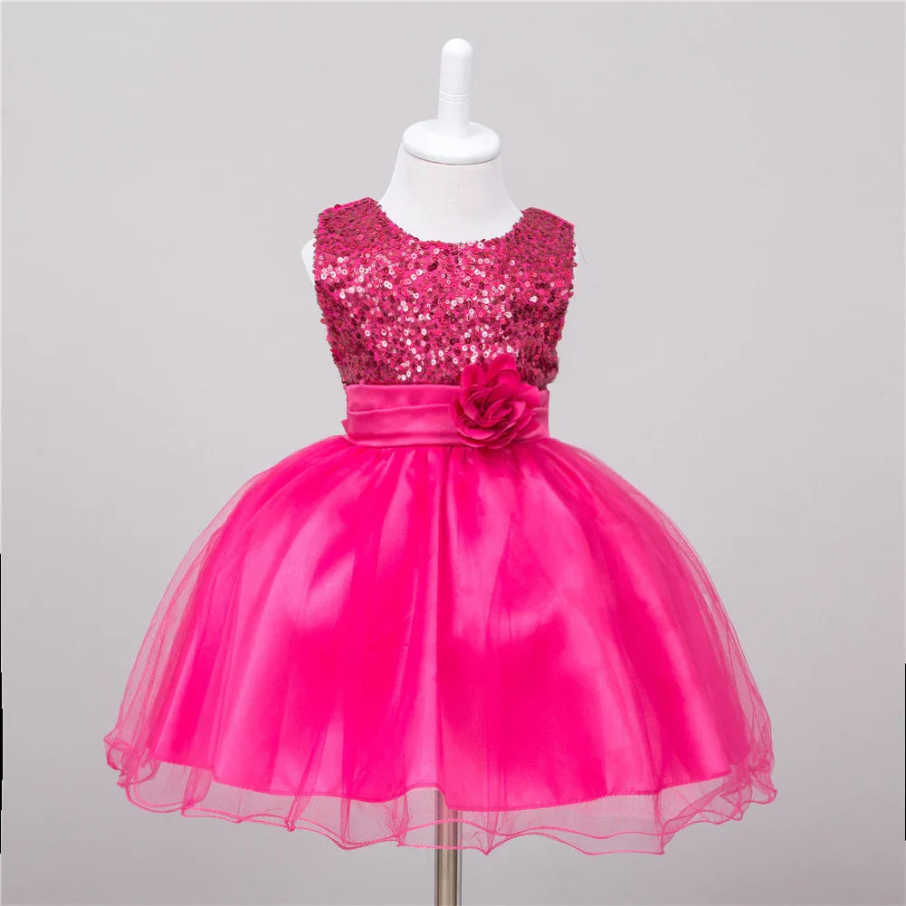 Bright pink sleeveless toddler dress with sequin top, satin waistband, flower embellishment, and tulle skirt