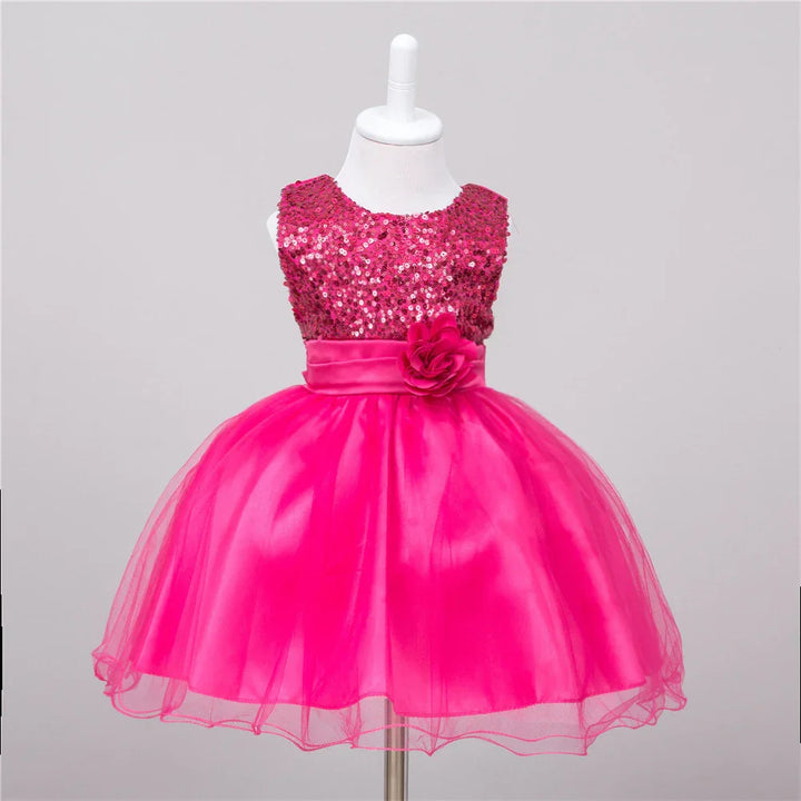 Bright pink sleeveless toddler dress with sequin top, satin waistband, flower embellishment, and tulle skirt