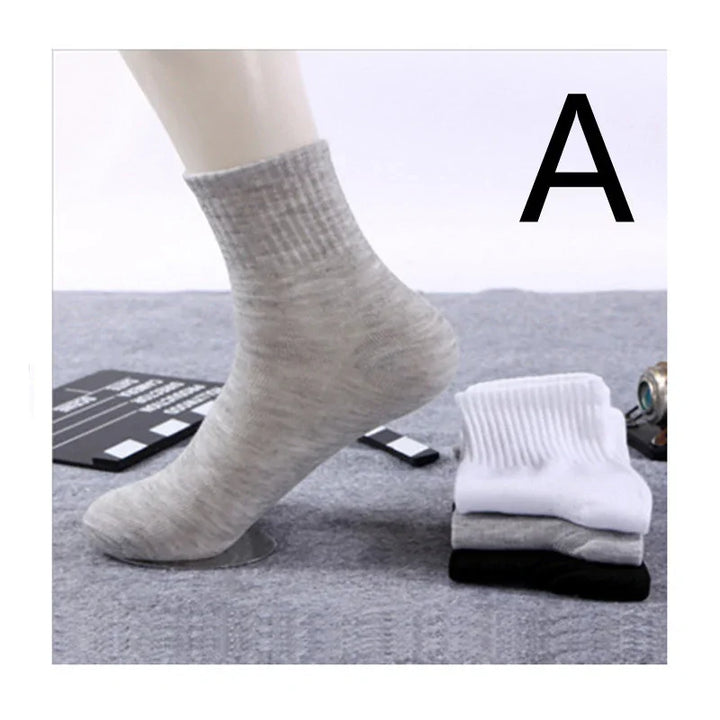 Light gray ribbed ankle sock on mannequin foot with folded white, gray, and black socks nearby