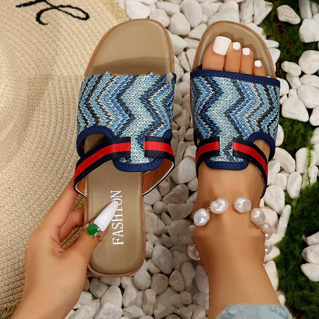 Blue zigzag patterned open-toe summer sandals on feet with white pedicure and pearl anklet on white stones