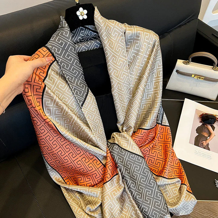Hand holding luxury silk scarf with geometric pattern in orange, grey, and beige on black sofa