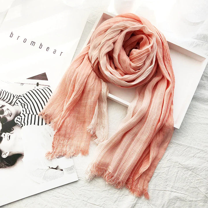 Soft peach striped scarf with frayed edges displayed on white textured fabric next to fashion magazine