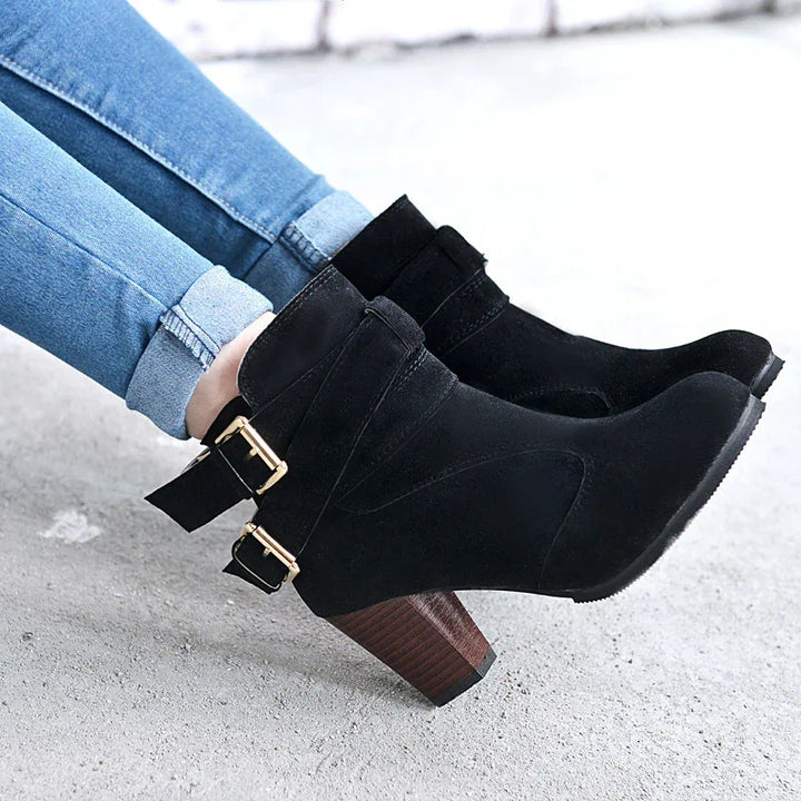 Black suede ankle boots with wooden block heels and gold buckle straps worn with rolled-up blue jeans