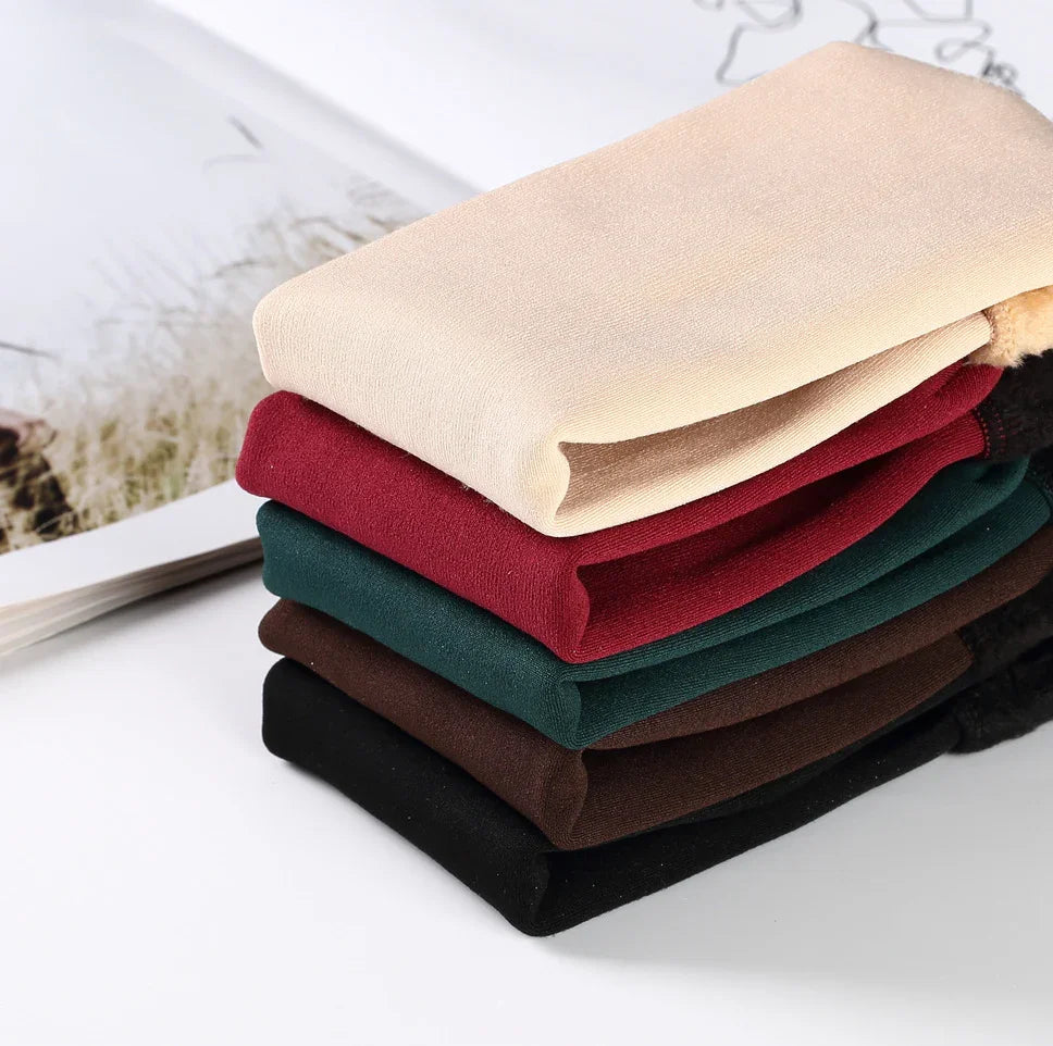 Stack of folded leggings in beige, red, green, brown, and black on white surface with open book
