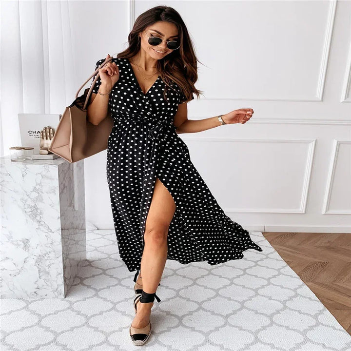 Woman wearing black polka dot wrap dress with slit, sunglasses, carrying beige handbag indoors