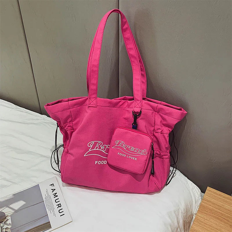 Bright pink tote bag with matching small pouch, white text 'Bread Food Lover', on bed near book