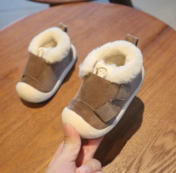 Soft brown baby shoes with white fluffy lining on wooden table, one held in hand