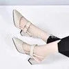 Woman's feet wearing beige Mary Jane block heel shoes with black pants on white background