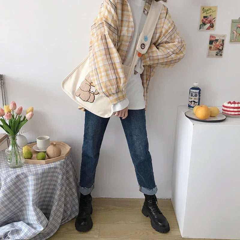 Casual outfit with yellow plaid jacket, rolled jeans, black boots, and beige tote bag with teddy bear design