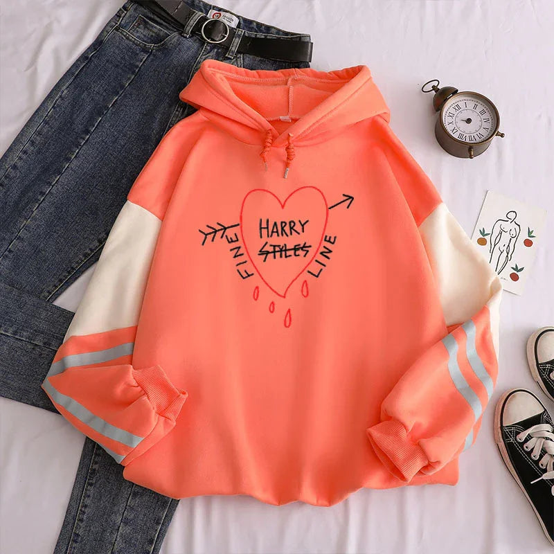 Coral orange hoodie with heart graphic and text 'Harry Styles Fine Line' paired with blue jeans and black belt