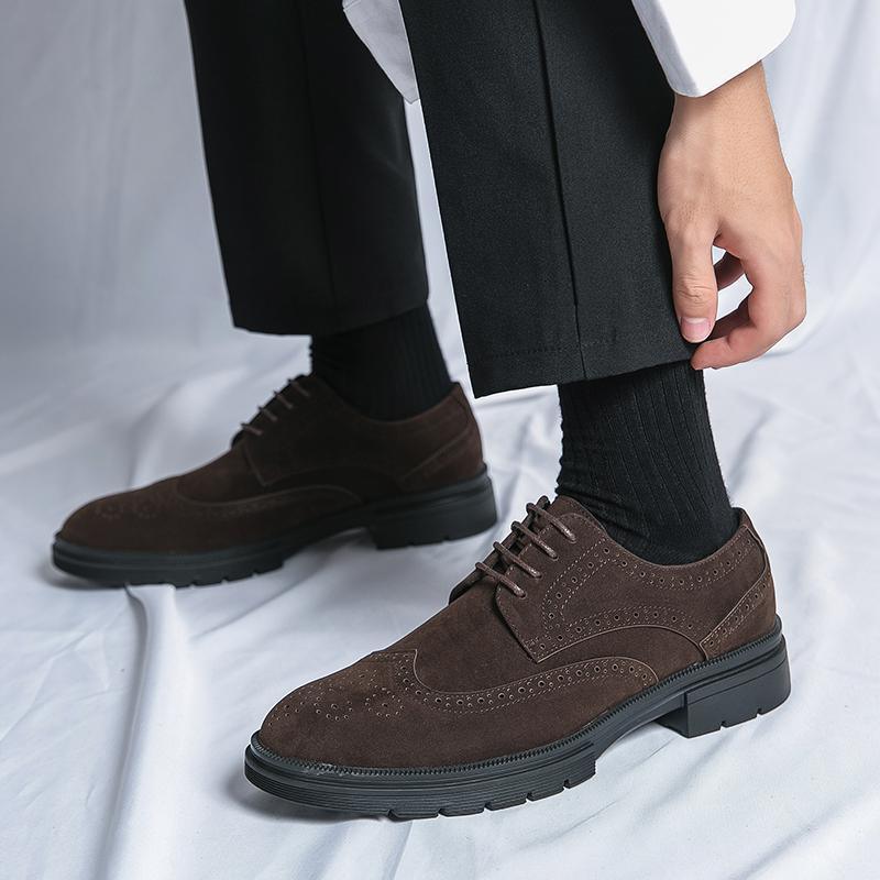 Close-up of dark brown suede men's dress shoes with brogue detailing worn with black socks and black pants