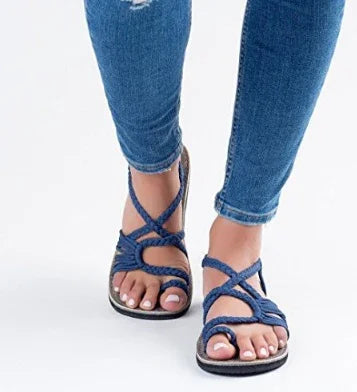 Close-up of feet wearing blue braided sandals paired with fitted blue jeans against a white background