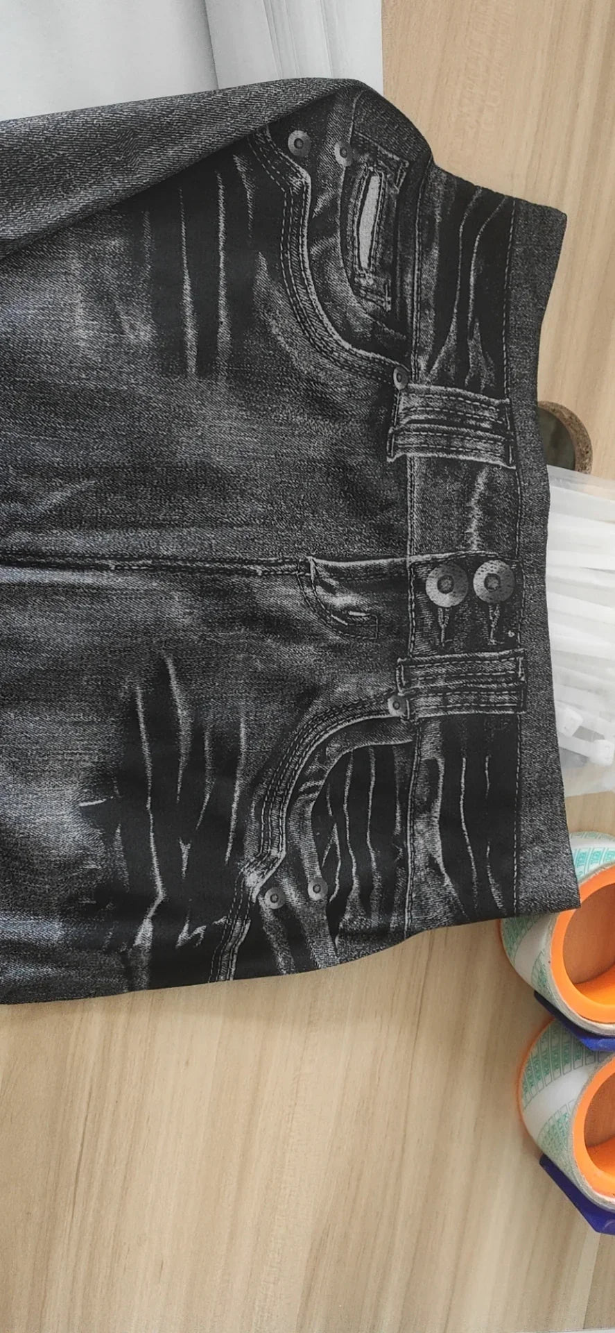 Close-up of printed denim jeans design with belt loops and double button detail on light wood surface