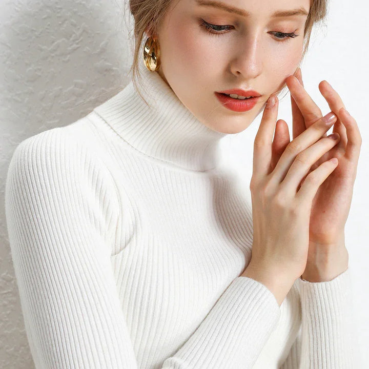Close-up of woman wearing white ribbed turtleneck sweater and gold hoop earrings, with natural makeup