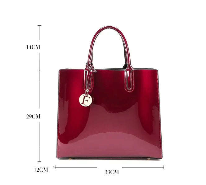 Glossy deep red patent leather tote bag with handles and gold charm against white background