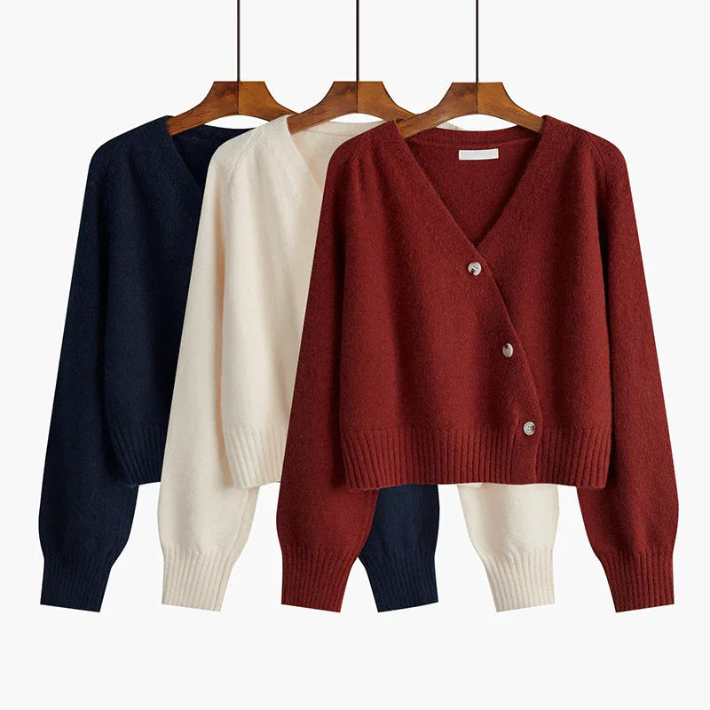 Three knitted V-neck buttoned cardigans in rust, cream, and navy blue on wooden hangers