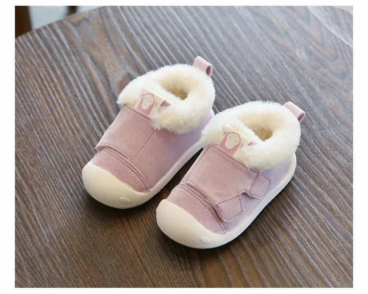 Pink baby shoes with white fur lining and soft soles on wooden surface