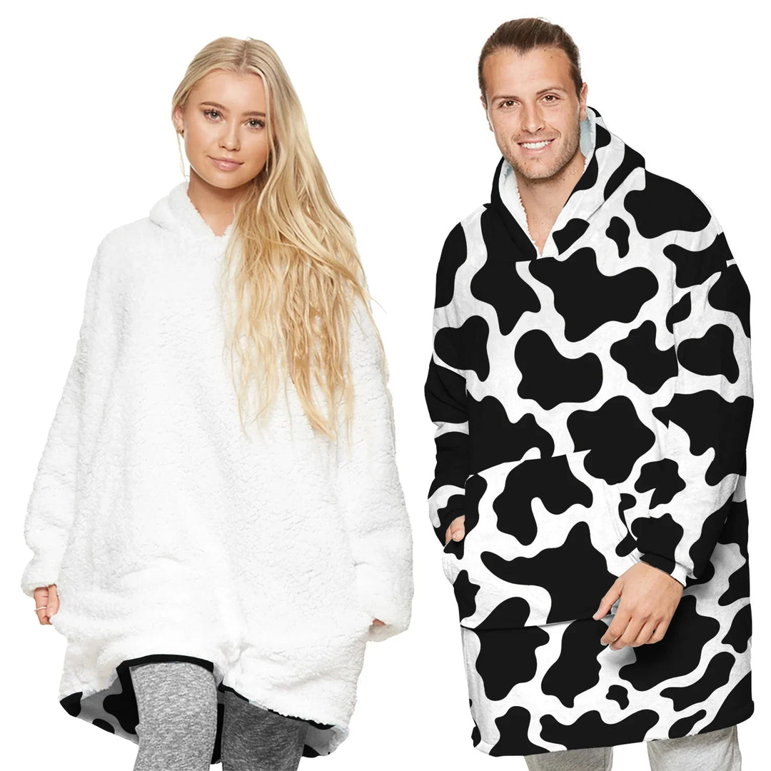 Man and woman wearing oversized cozy hooded blankets, woman in white, man in black and white cow print