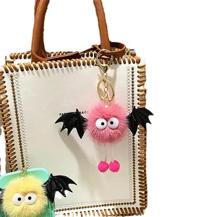 White leather tote bag with brown whipstitch edges and two fuzzy bat keychains in pink and yellow