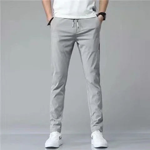 Man wearing light gray slim-fit jogger pants with white sneakers and a white t-shirt against a gray background