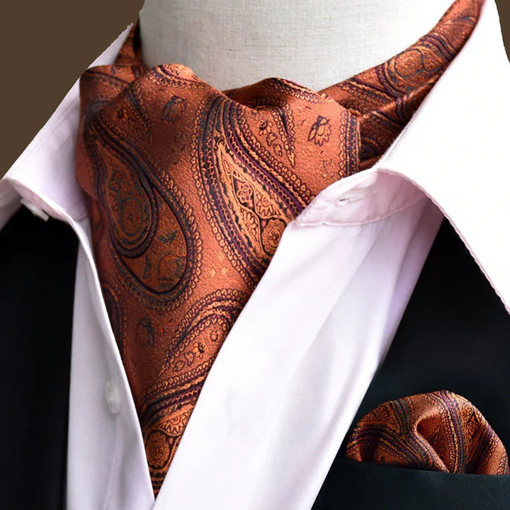 Orange paisley ascot tie and matching pocket square on white dress shirt and black suit