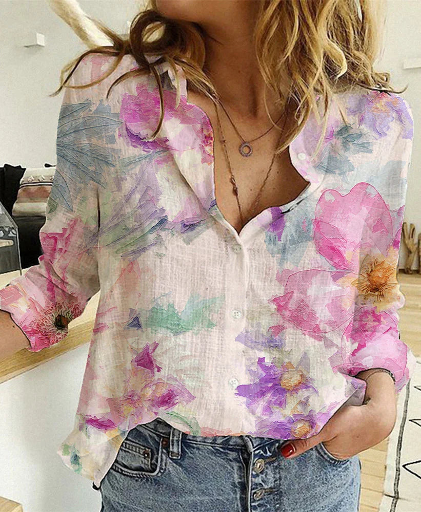 Woman wearing lightweight floral button-up blouse with pink and purple flowers and blue jeans indoors