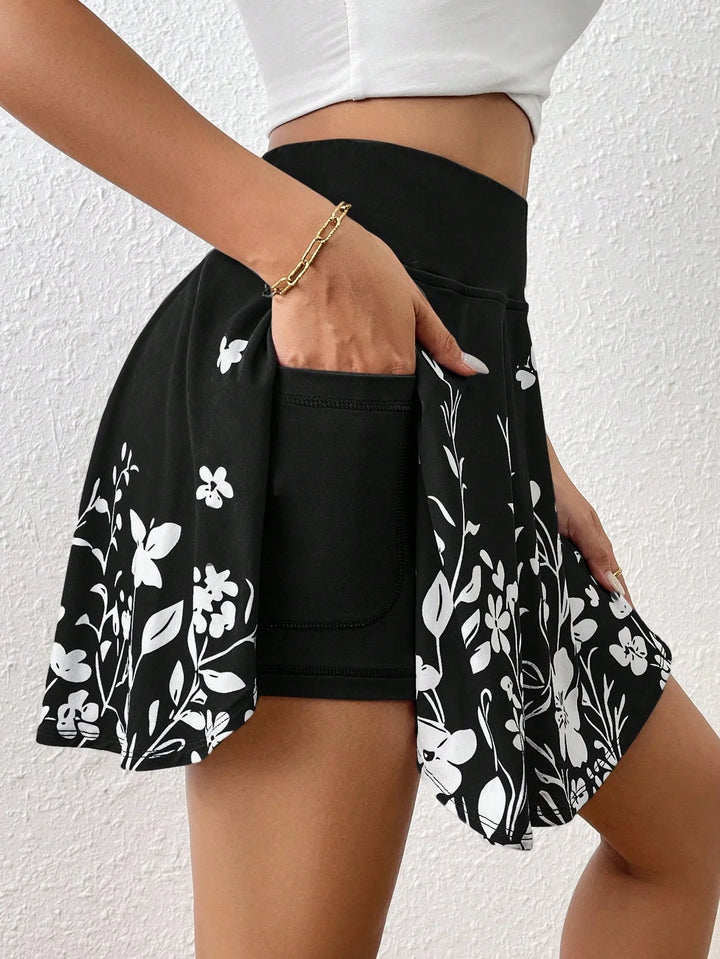 Woman wearing black floral skort with built-in shorts and white floral print, posing against white wall