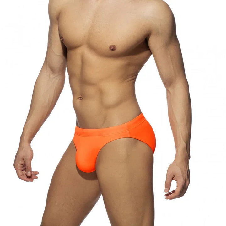 Muscular man wearing bright orange men's briefs underwear on white background