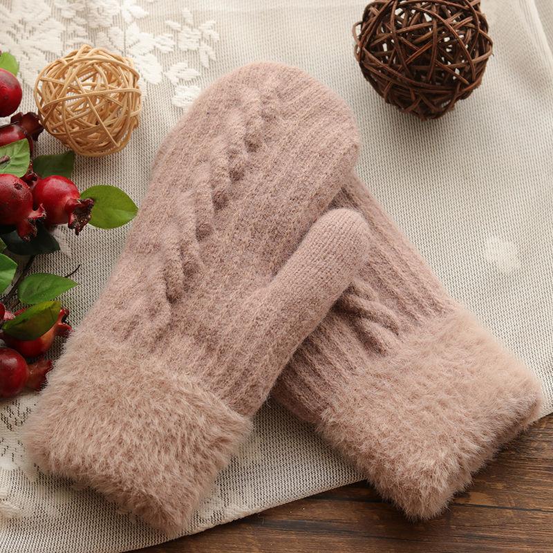 Soft pink knitted winter gloves with fuzzy cuffs on a lace and wooden surface with decorative berries and wicker balls