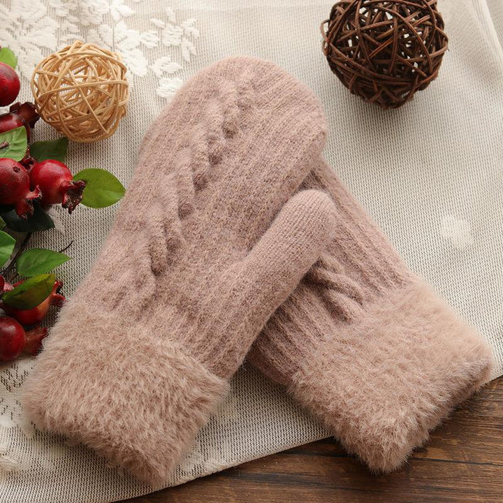 Soft pink knitted winter gloves with fuzzy cuffs on a lace and wooden surface with decorative berries and wicker balls