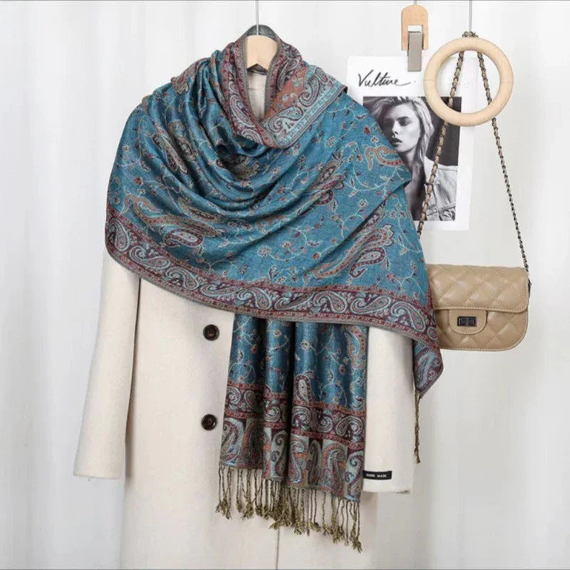 Blue paisley patterned scarf draped over cream coat with buttons, beige quilted chain-strap bag hanging nearby