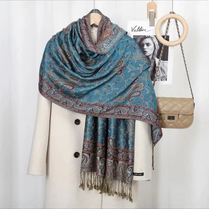 Blue paisley patterned scarf draped over cream coat with buttons, beige quilted chain-strap bag hanging nearby