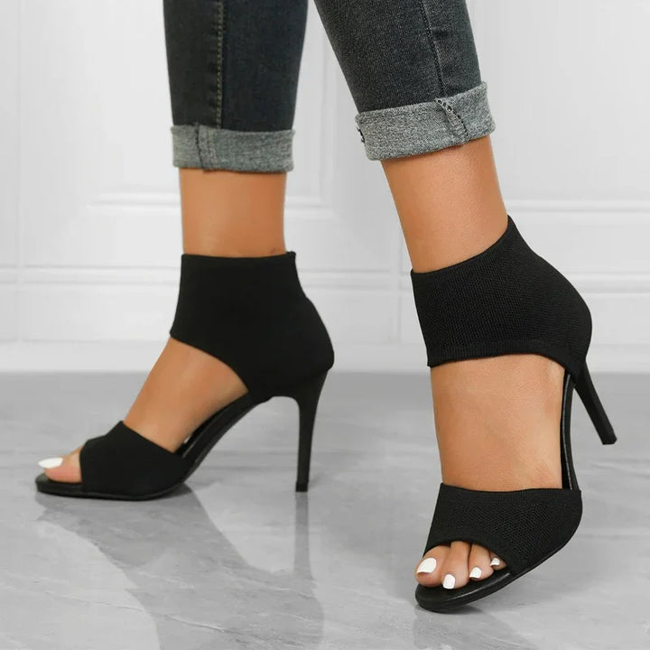 woman wearing black open-toe high heel ankle boots with rolled-up dark gray jeans
