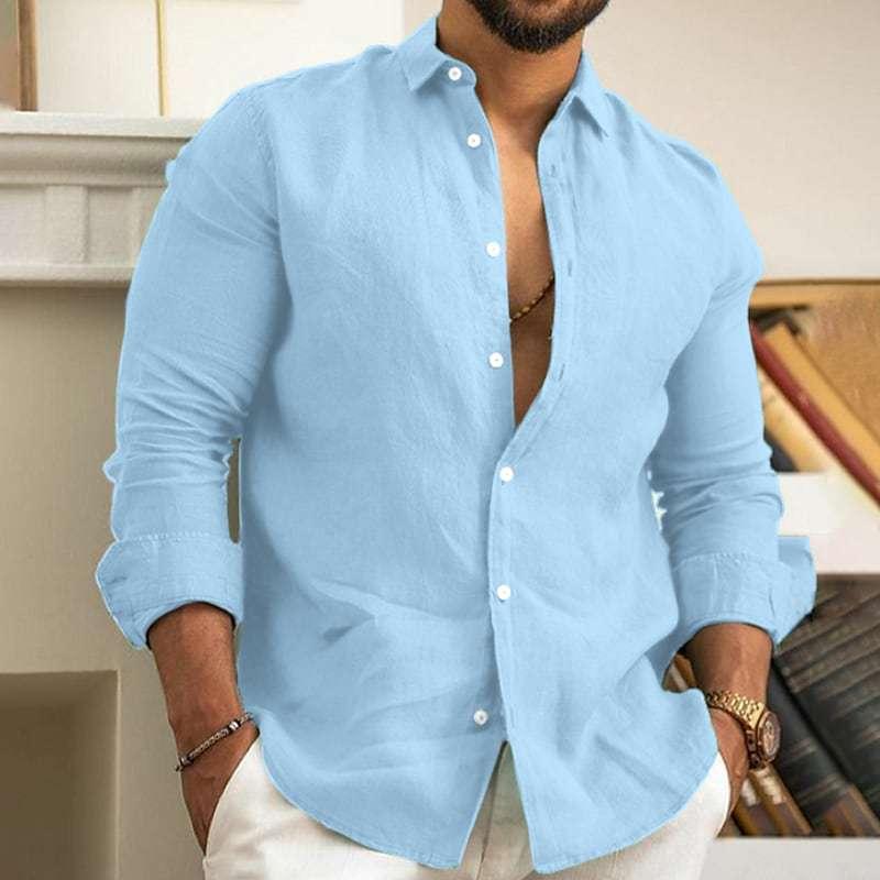 Man wearing light blue casual linen shirt with white buttons, sleeves rolled up, and white pants indoors