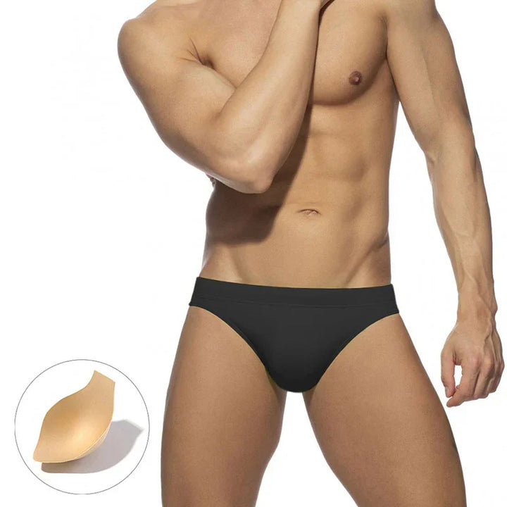Fit male model wearing black seamless bikini underwear on white background with beige underwear padding detail