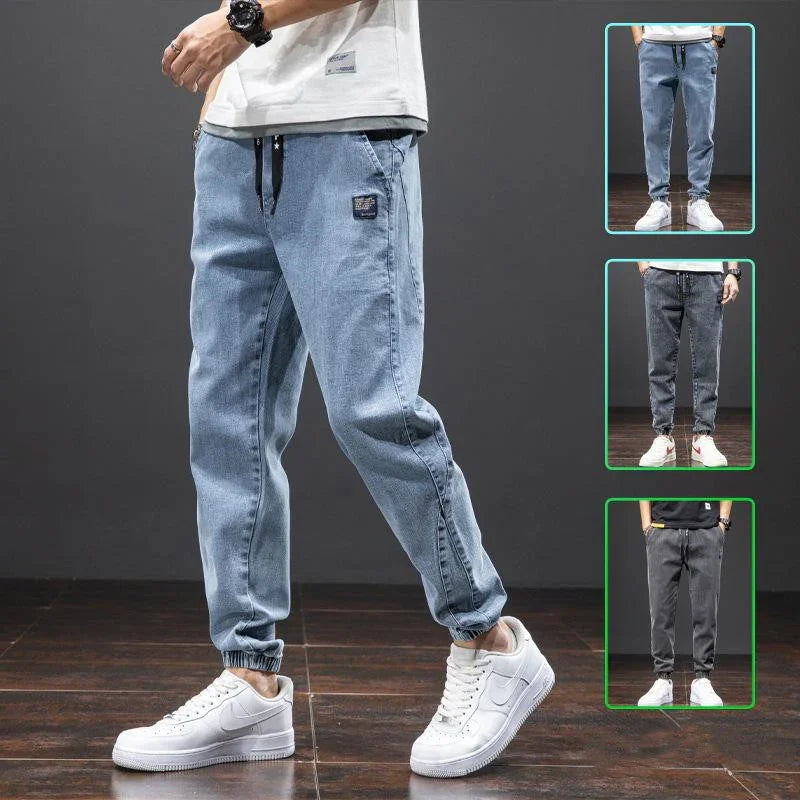 Man wearing light blue denim jogger pants with elastic cuffs and white sneakers on wooden floor