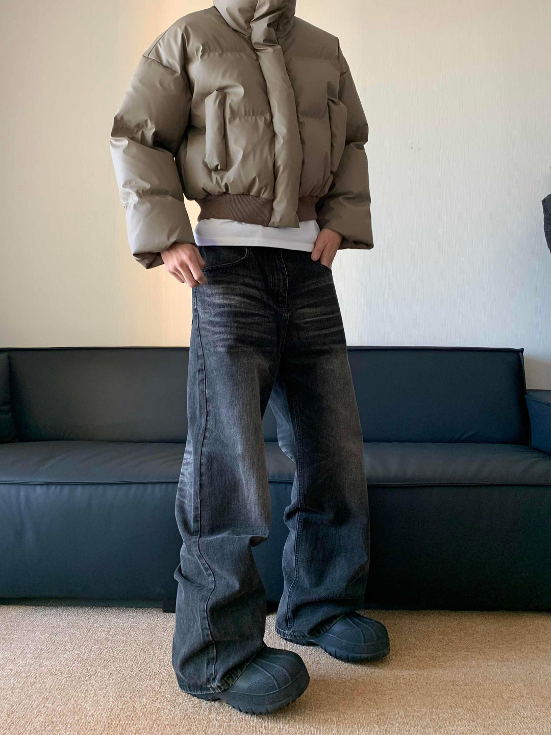 Person wearing taupe puffer jacket, black wide-leg jeans, and black chunky shoes indoors